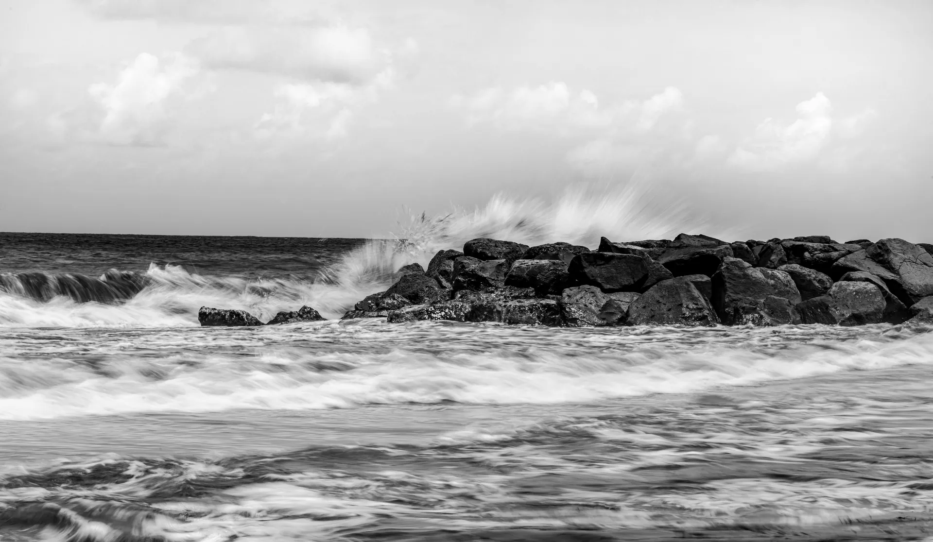 Black and white image of ocean waves crashing against rocky shore, creating a moody seascape.